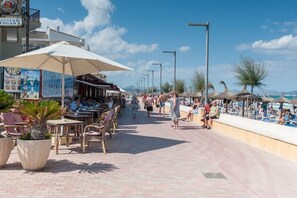 Un paseo marítimo con mesas al aire libre, sombrillas y una playa al fondo.