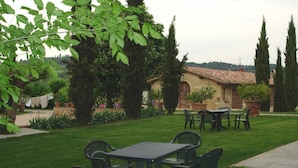 Un jardin avec une table et des chaises, un bâtiment avec un toit en tuiles et de grands arbres.