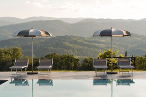 Area piscina con lettini e ombrelloni, con vista su un paesaggio montuoso.