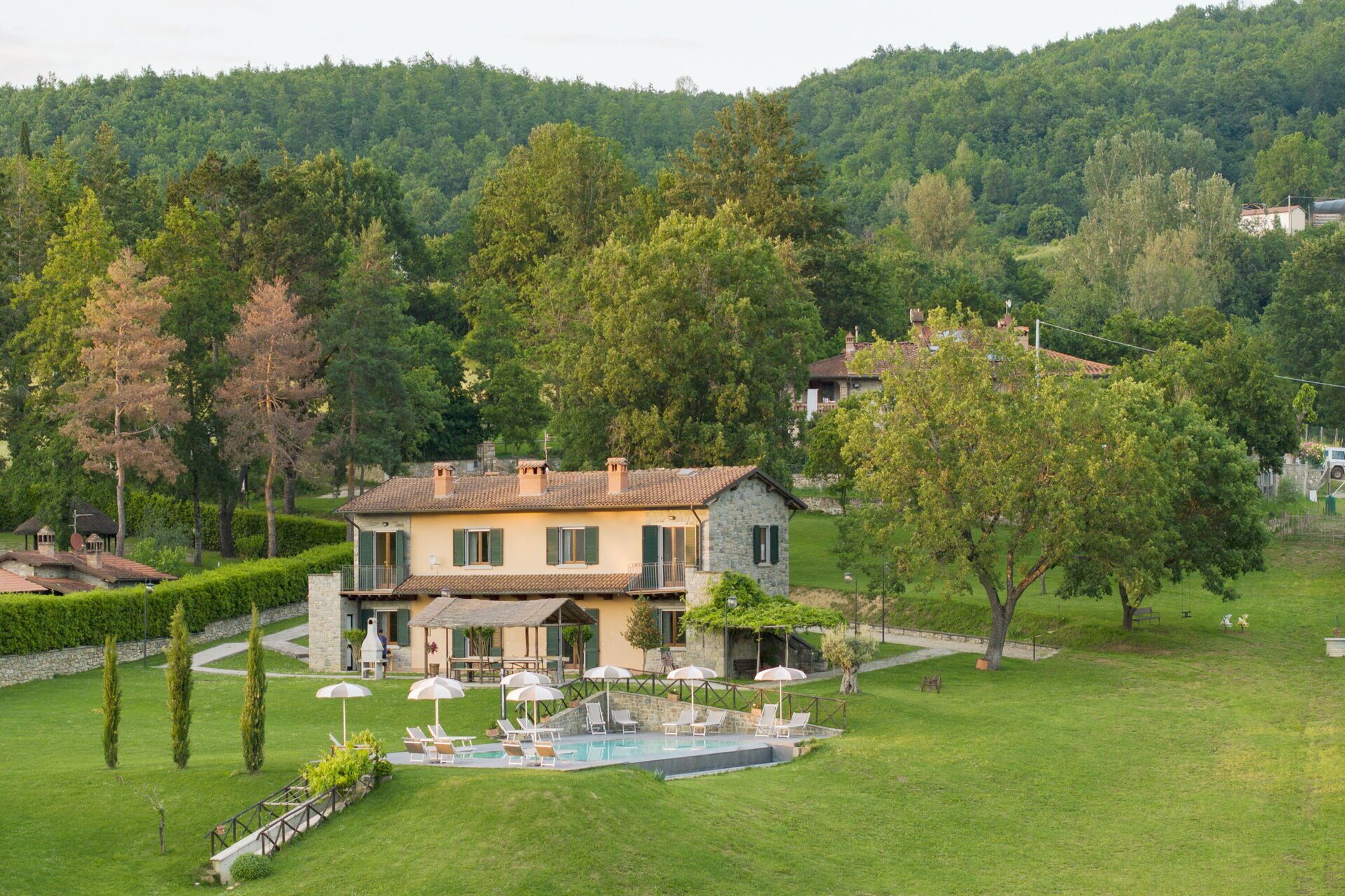 A two-story stone house with a swimming pool, surrounded by a well-maintained lawn and trees.