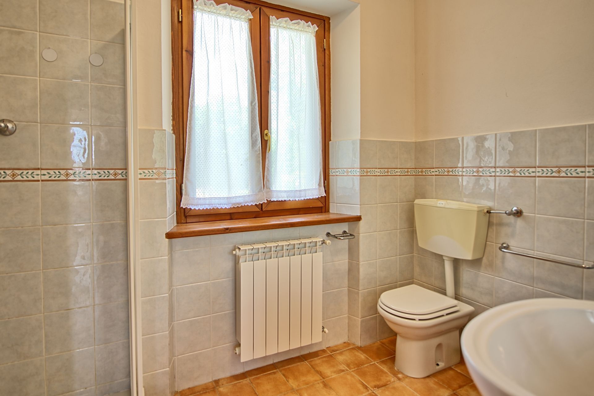 A bathroom with a toilet, a radiator, and a window with curtains.