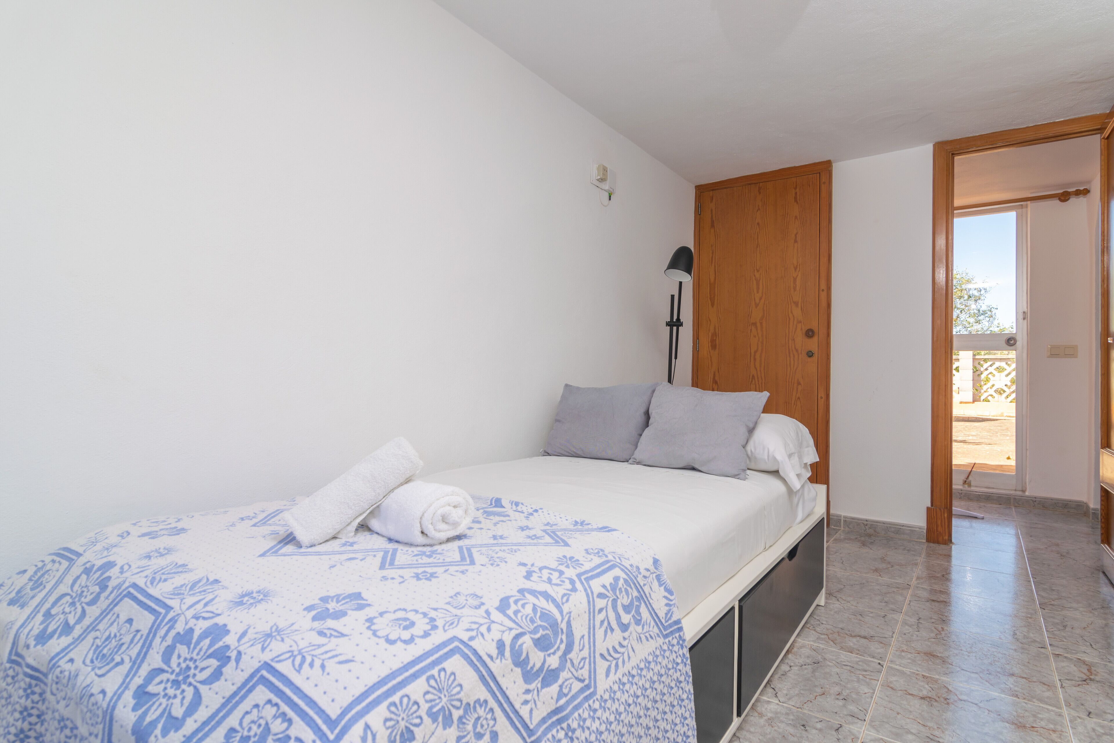 Un dormitorio con una cama, una puerta de madera y vistas al exterior.