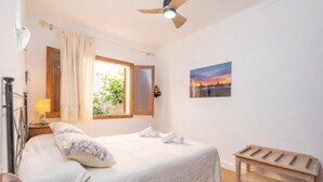 A bedroom with a bed, a window with curtains, a ceiling fan, a bedside table, and a painting on the wall. - CAN PONS - Chalet with terrace in Ca'n Picafort. Free WiFi (Can Picafort)