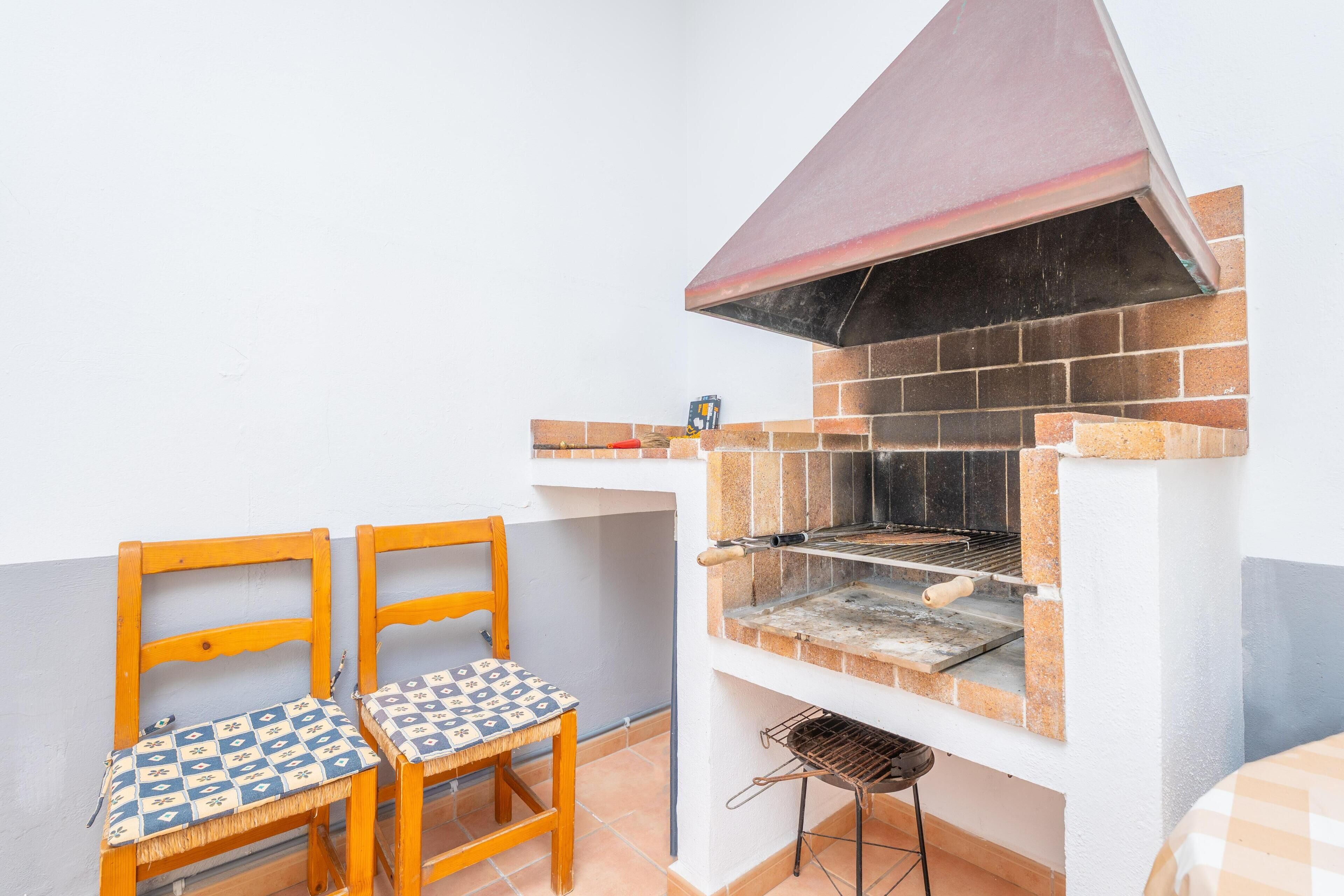 Un pequeño espacio cocina exterior con una parrilla, dos sillas de madera y una mesa.