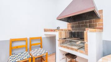 Un pequeño espacio cocina exterior con una parrilla, dos sillas de madera y una mesa.