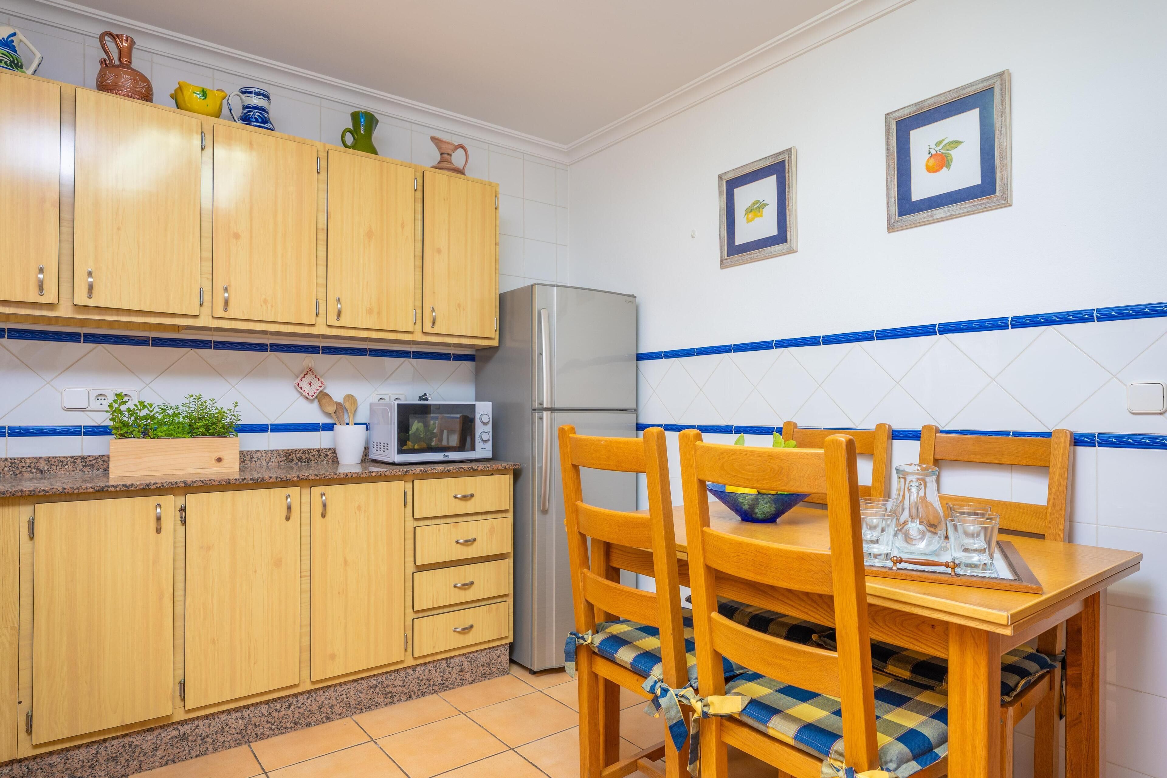 Una cocina con armarios de madera, un microondas, un refrigerador y una mesa de comedor con sillas.