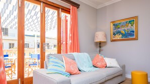 A room with a grey sofa, colorful cushions, a yellow ottoman, a painting on the wall, and a view through a glass door. - CAN PONS - Chalet with terrace in Ca'n Picafort. Free WiFi (Can Picafort)