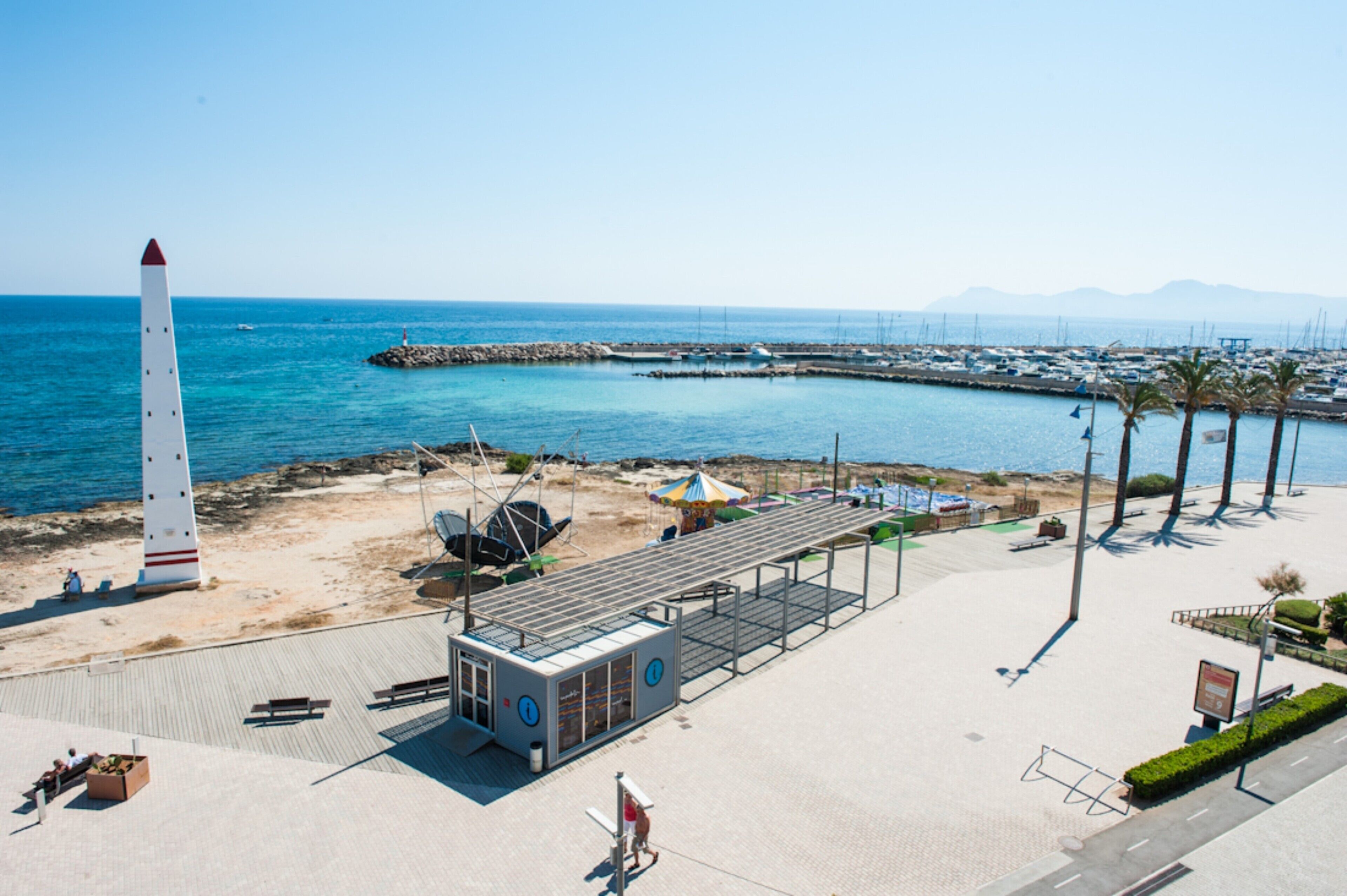 Um calçadão costeiro com um farol, praia e marina.