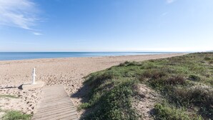 Une plage avec une promenade en bois qui mène à l’eau, des dunes herbeuses et un ciel bleu dégagé.