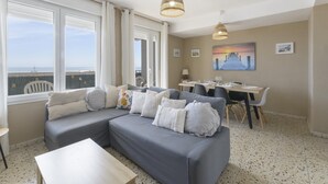 Un salon avec un canapé gris, une table à manger et un tableau représentant un coucher de soleil.
