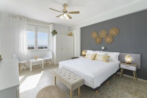 Une chambre à coucher avec un lit, des tables de chevet, un banc, un ventilateur de plafond et une vue sur la mer.