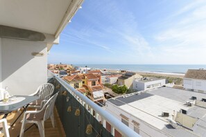 Un balcon avec une table et des chaises, donnant sur une plage et des immeubles.