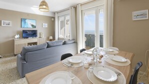 Un coin repas avec une table en bois dressée pour quatre personnes, un canapé gris et un téléviseur en arrière-plan.