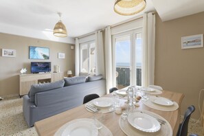 Un coin repas avec une table en bois dressée pour quatre personnes, un canapé gris et un téléviseur en arrière-plan.