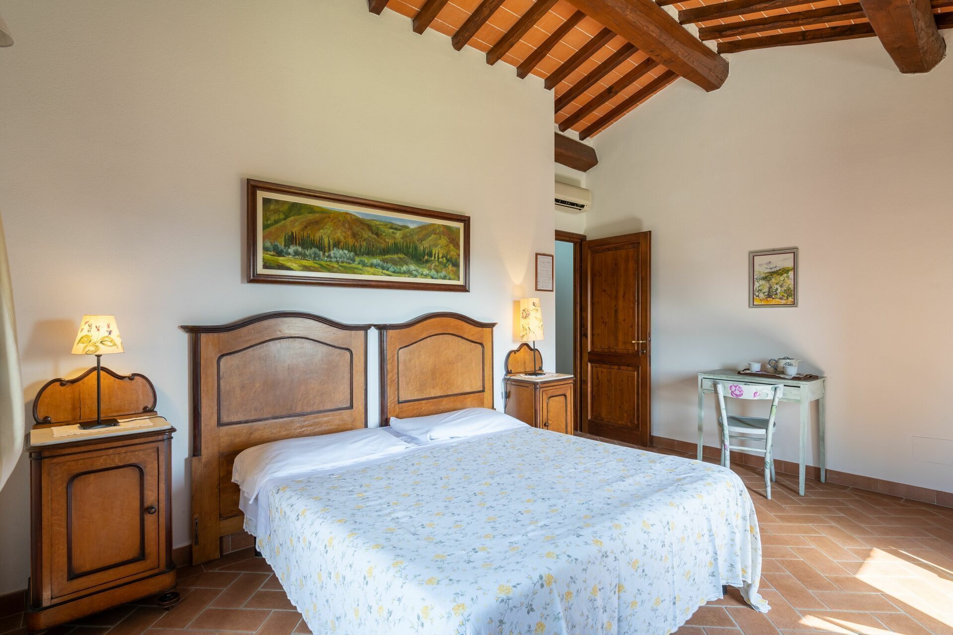 Une chambre à coucher avec un lit, un bureau et une chaise. Il y a un tableau au mur et une lampe sur la table de chevet.