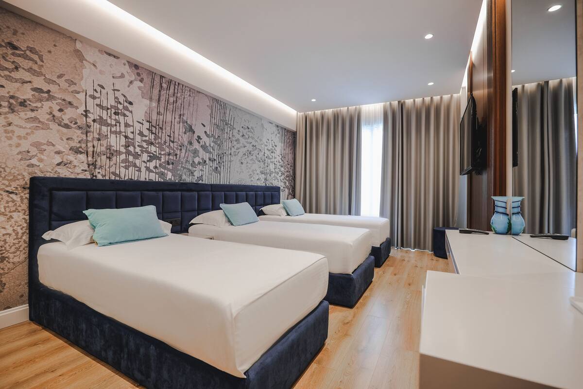 A modern hotel room with two beds, a large wall mural, a flat-screen TV, and a wooden floor.