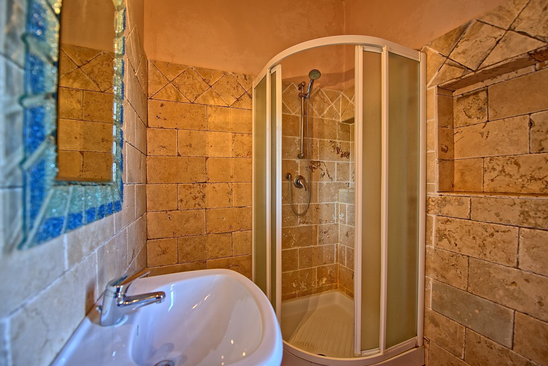 Een badkamer met een douche, wastafel en een wand betegeld met mozaïek.