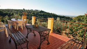 Una terraza con una mesa y sillas, un banco y vistas a un paisaje montañoso.
