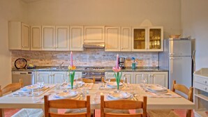 Una cocina con armarios blancos, salpicadero de ladrillo y una mesa de comedor con platos, vasos y una vela.