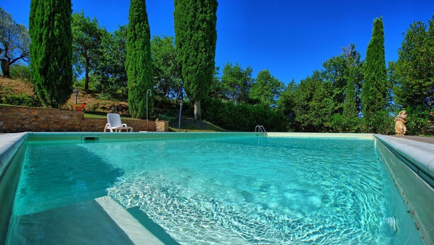Una piscina cristalina con una pared de piedra y una silla blanca.