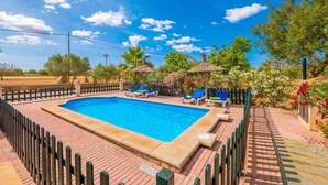 A rectangular swimming pool with a wooden deck, surrounded by a black fence.