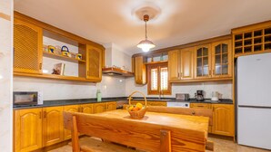 A kitchen with wooden cabinets, a marble countertop, a wooden dining table with a bench, and a white refrigerator.
