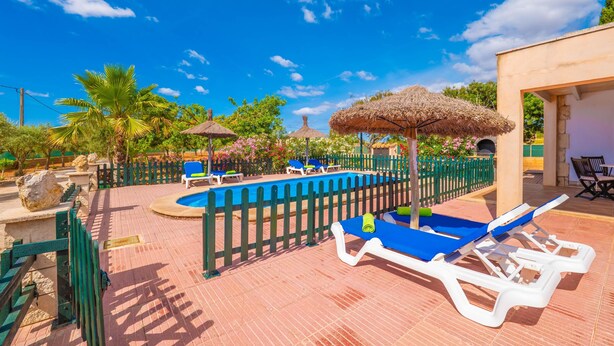 A pool area with lounge chairs, a pool, and a thatched umbrella.