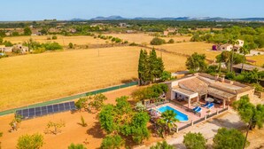 A villa with a swimming pool, surrounded by fields and trees.