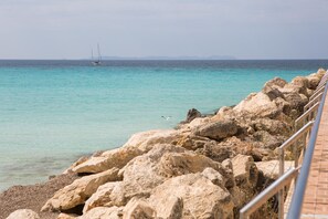 A rocky shoreline with a clear view of the sea and a sailboat in the distance.
