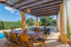 An outdoor patio with a wooden table and chairs, a pool, and lounge chairs.