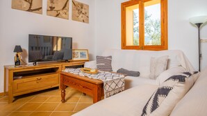 A living room with a television, wooden furniture, a window, and artwork on the wall.