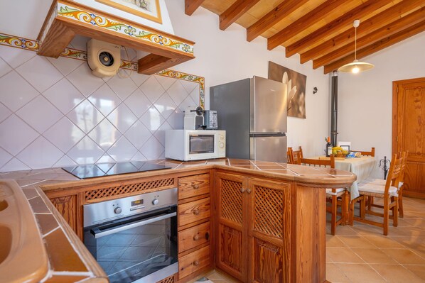 A kitchen with wooden cabinets, a microwave, a refrigerator, and a dining area with chairs.