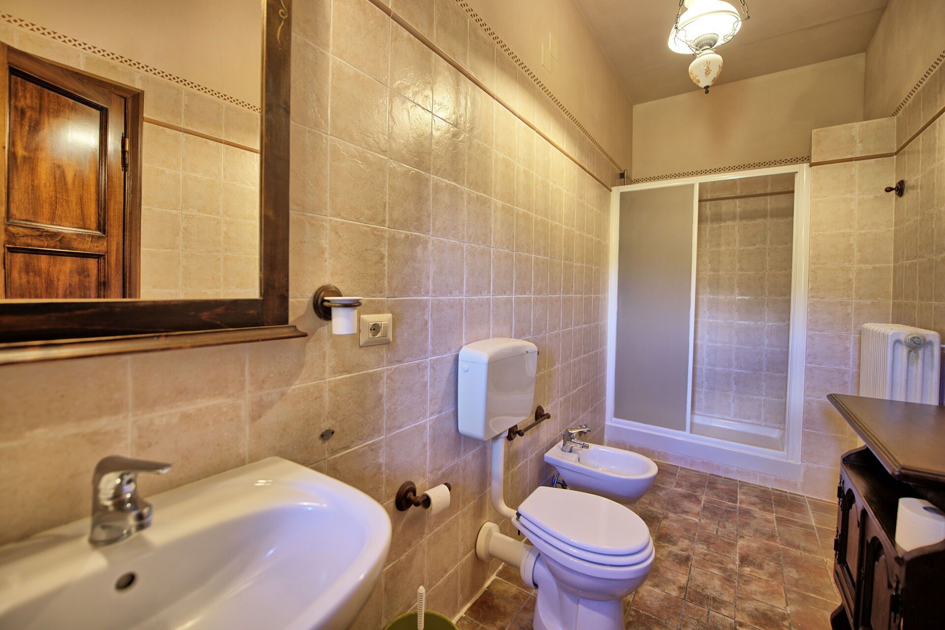 Un baño con lavamanos, dos inodoros, ducha y espejo.