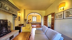 A living room with a sofa, a wooden table, and a yellow armchair. There is a billiards table in the background. - Villa Lo Scoiattolo - Holiday Country Villa with private swimming pool in Casentino Valley, Tuscany (Subbiano)