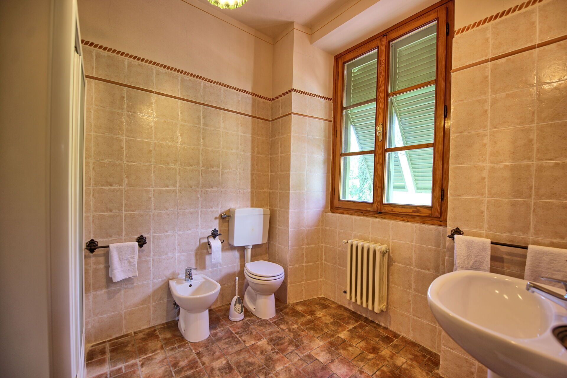 A bathroom with a toilet, bidet, sink, and a window with blinds.