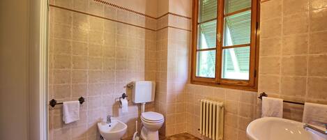 A bathroom with a toilet, bidet, sink, and a window with blinds.