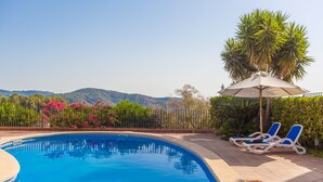 A swimming pool with blue water, surrounded by a fence, and two lounge chairs with a beach umbrella. - VILLA BELLAVISTA – Villa with private pool in Campanet with free WiFi (Campanet)