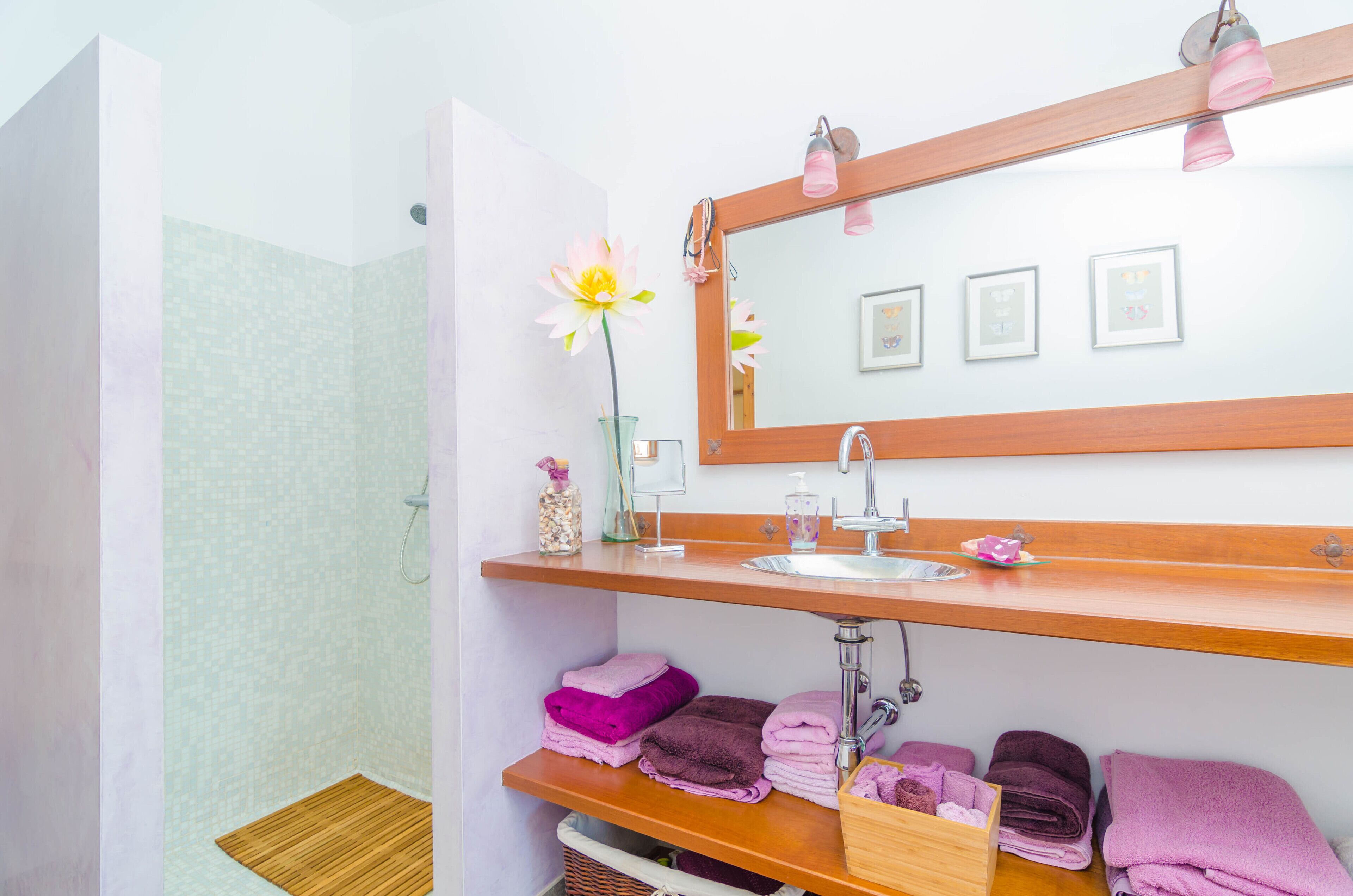 A bathroom with a shower, a sink with a mirror, and shelves with folded towels.