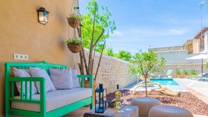 Une terrasse avec un canapé vert, des poufs en osier, une table en bois avec des verres à vin, une lanterne et des paniers suspendus.