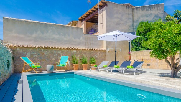 Une piscine entourée de chaises longues et de parasols, le tout bordé de murs en pierre et agrémenté d’un arbre.
