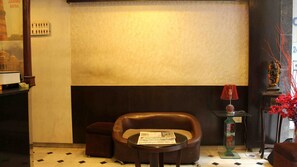A lobby with a sofa, a small table with a newspaper, a lamp, and a decorative vase. - Anmol Hotels (New Delhi)