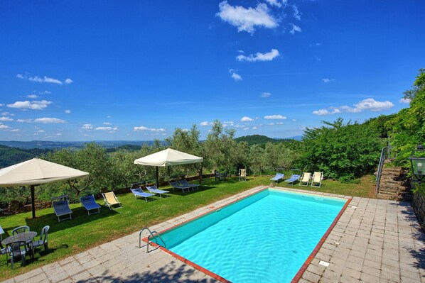 Un espace piscine agrémenté de chaises longues et de parasols, entouré de verdure et offrant une vue sur des collines lointaines.