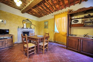 A dining area with a wooden table and chairs, a fireplace, and a kitchen area with cabinets and a stove.
