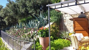 A patio with a stone wall, a wooden door, a metal fence, and various potted plants.