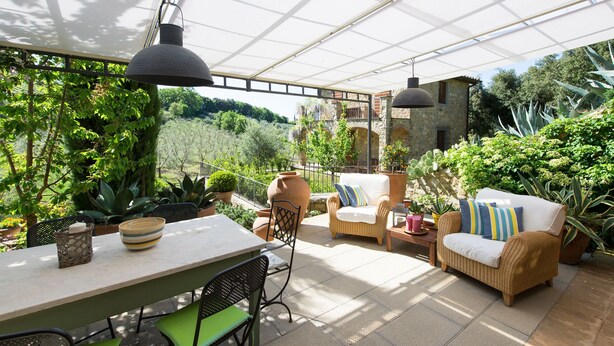 A covered patio with wicker furniture, a table with a bowl, and potted plants.