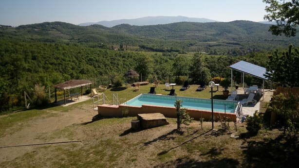 Uma área de piscina com espreguiçadeiras e uma estrutura com telhado de palha, cercada por vegetação exuberante e colinas ao fundo.