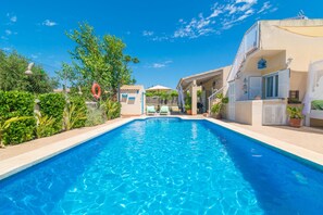 A swimming pool with a clear blue water, surrounded by greenery and buildings.