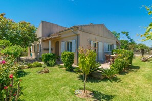 A two-story house with a garden, a patio with a table and chairs, and a small pool.