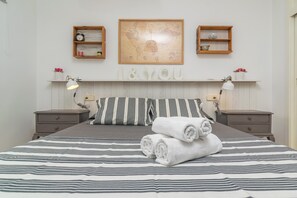 A neatly made bed with striped bedding, two bedside tables with lamps, a world map on the wall, and a shelf with decorative items.