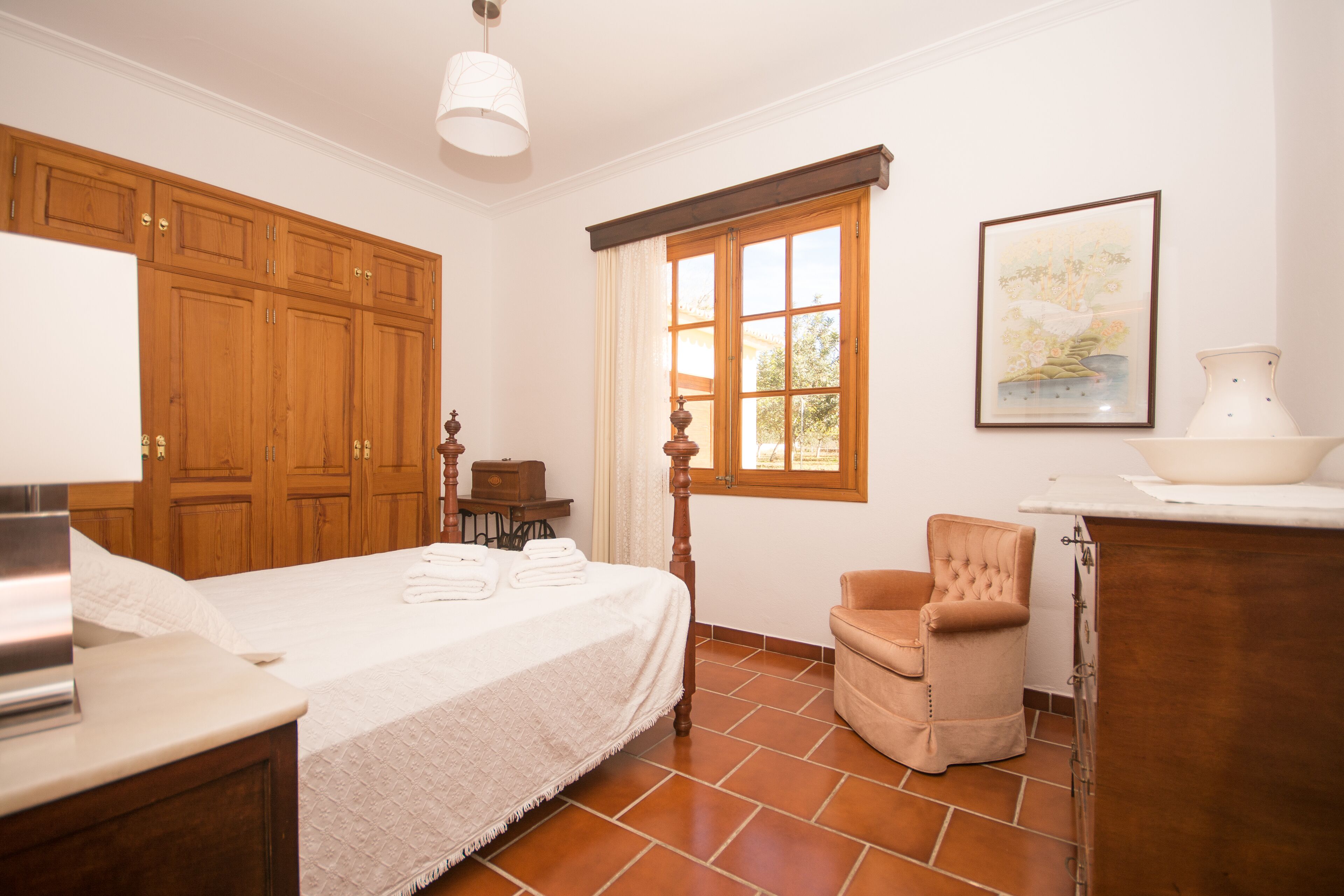Un dormitorio con una cama grande, un armario de madera, una silla, un escritorio y una ventana con cortinas.